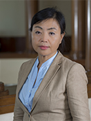 Woman with dark short hair in a blue shirt and tan blazer looking into the camera